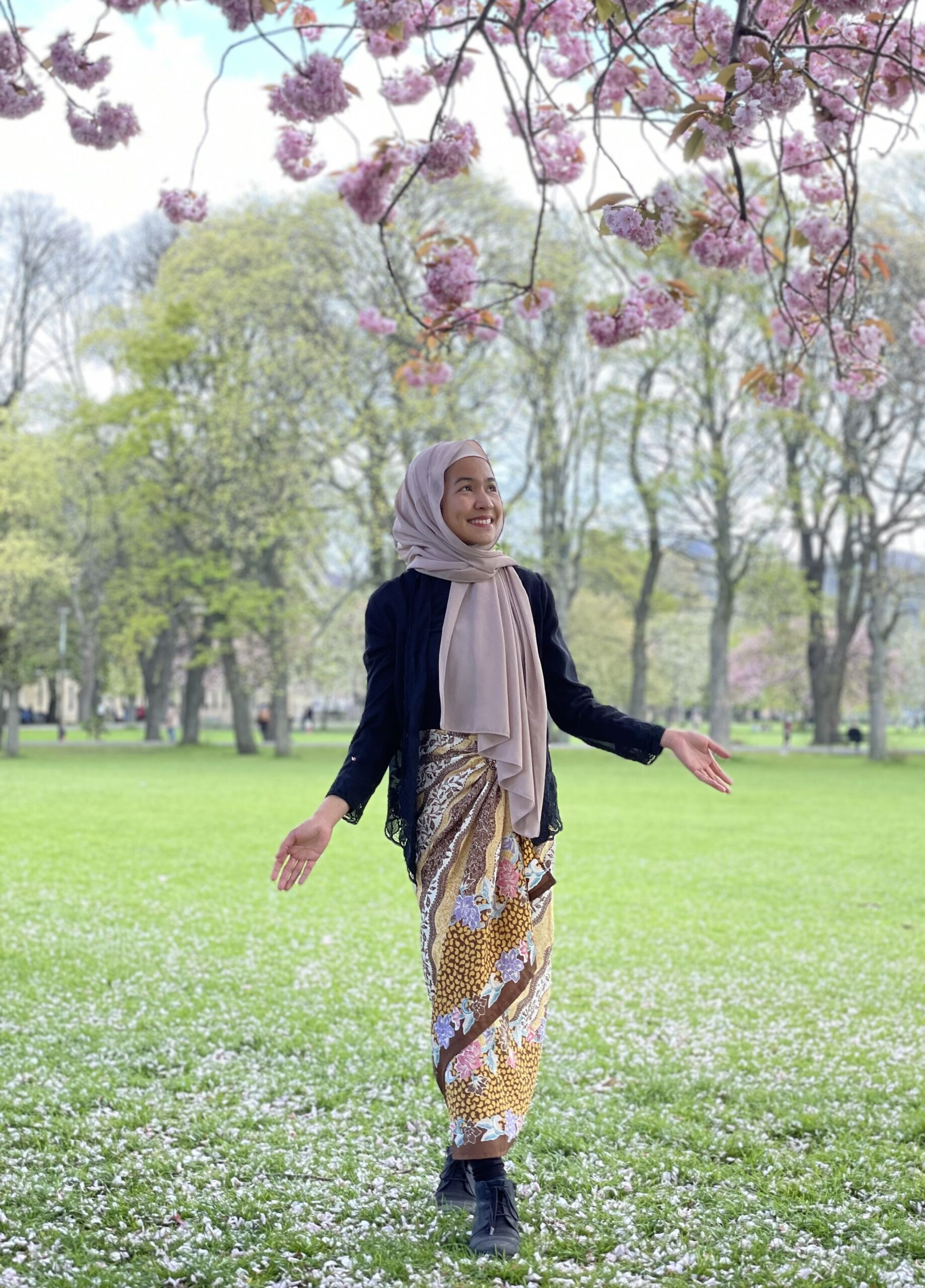 Sofea in a pink scarf underneath some cherry blossoms